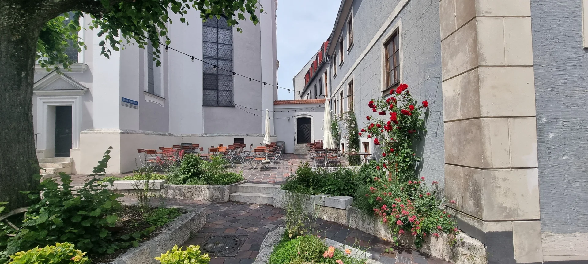 Außenterasse des Cafés "zum Rufer", welcher an der gegenüberliegenden Straßenseite der Amalienstraße am Bischof-Simpert-Platz an der Peterskirche gelegen ist.